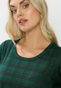 Top a scacchi verdi con scollatura tonda, texture morbida e vestibilità casual, che presenta un motivo di quadrati verde scuro e chiaro.