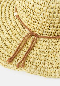 Sombrero de paja en color amarillo claro con ala ancha, que presenta un cordón marrón con detalle de tope, mostrando un patrón texturizado de tejido.