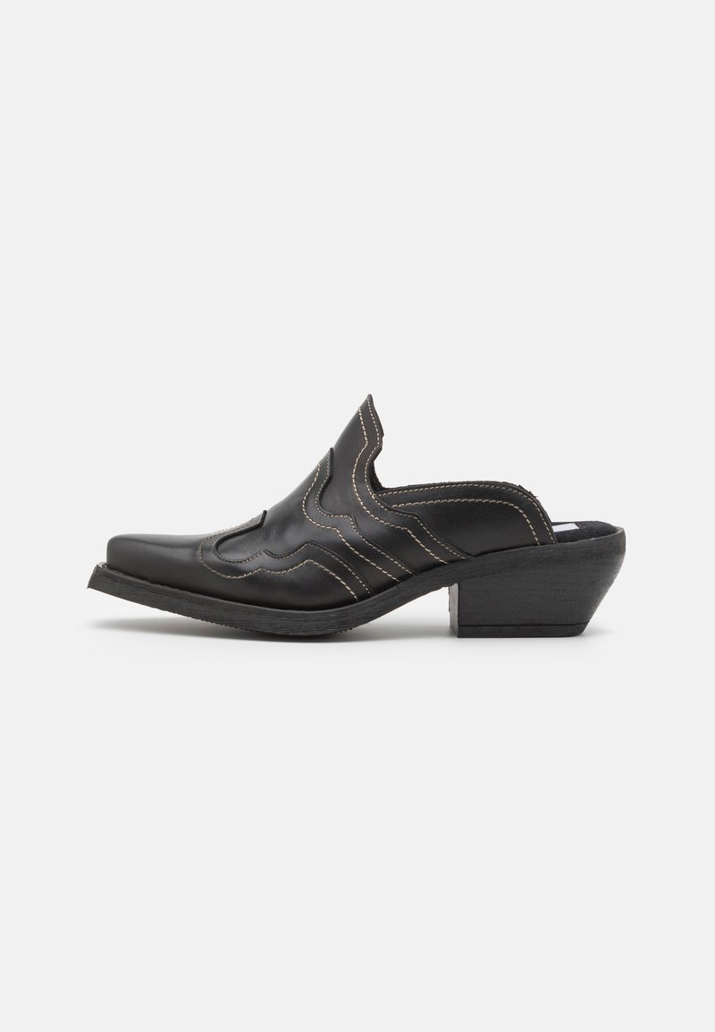 Mule en cuir noir avec bout pointu, dessus festonné avec coutures blanches, et talon empilé incliné.