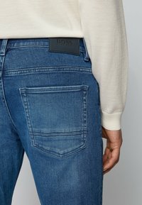 Modré džíny z denimu s mírně vybledlým vzhledem, na pase s černou koženou etiketou a dvěma zadními kapsami se šitým detailem.