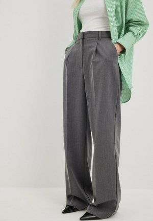 Gray high-waisted trousers with pleats, made of textured fabric. Features a wide leg design and slanted side pockets, paired with a green striped shirt.