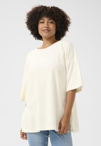 Krämfärgad oversized t-shirt i mjukt material med bred rund halsringning och korta ärmar, tillsammans med blå denimjeans.