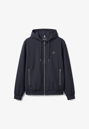 Marineblauwe capuchonjas met ritssluiting, trekkoorden, twee voorzakken met rits, elastische manchetten en zoom, en een klein vierkant logo op de borst.