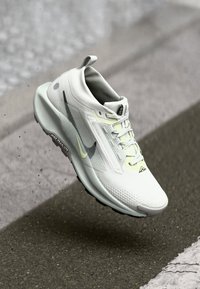 Baskets de sport blanches avec tige en mesh texturé, accents noirs et jaunes, et semelle rembourrée. Présente un design moderne et élégant.