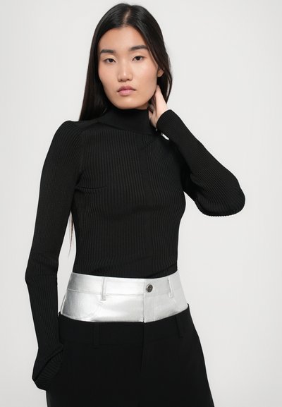 Bluză neagră cu guler înalt și mâneci lungi, asortată cu pantaloni negri care au un brâu argintiu lucios. Textură netedă cu un design ajustat.