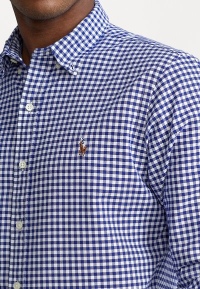 Blue and white gingham button-down shirt with a pointed collar, featuring a small embroidered logo on the chest and standard white buttons.