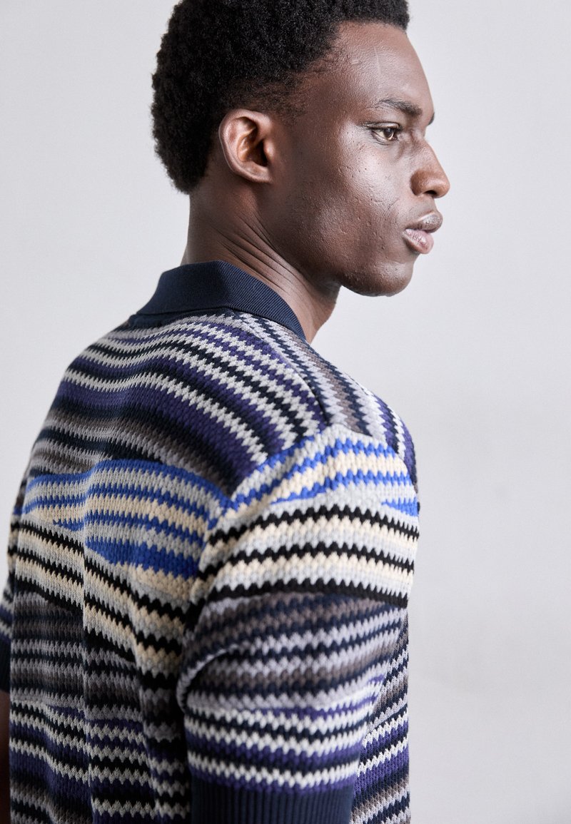 Maglione da uomo lavorato a maglia con un motivo a zigzag nei colori blu, nero, grigio e crema, con colletto scuro e tessuto texturizzato.