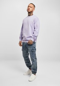 Felpa crewneck di colore viola chiaro abbinata a joggers cargo blu sbiaditi. I pantaloni sportivi presentano tasche e polsini elasticizzati. Sneakers bianche completano il look.