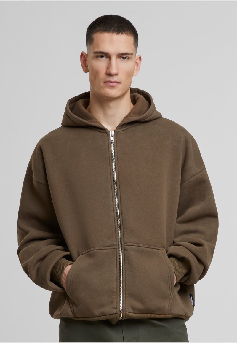 Brauner Reißverschluss-Hoodie aus weichem Stoff, mit einer großzügigen Kapuze und Vordertaschen. Mit einem glatten Reißverschluss und gerippten Bündchen.