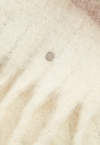 Tissu léger beige, doux et moelleux avec une texture subtile. Présente un bouton métallique argenté, rond, au centre avec une surface plate.