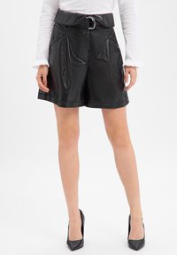 Czarne szorty ze sztucznej skóry z szerokim pasem, szlufkami na pasek i srebrną klamrą. Posiadają przednie kieszenie i gładką fakturę.