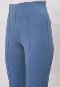Leggings bleus en matériau extensible avec une texture lisse. Équipés de coutures verticales sur les côtés et d'une taille haute.