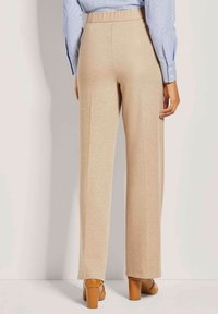 Beige weite Hosen aus einem glatten, strukturierten Stoff. Der Bund ist elastisch, und die Hose hat seitliche Nähte sowie einen sauberen Saumabschluss.