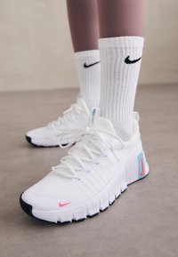 Zapatillas deportivas blancas con un upper de tela texturizada, acentos en rosa y azul, y una gruesa suela de goma negra, combinadas con calcetines blancos de canalé.