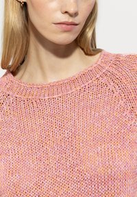 Knit sweater in pastel pink and orange tones, featuring a wide neckline and textured fabric with a loose stitch design.