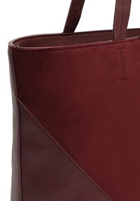 Arti vininis dviejų atspalvių tamsiai raudonos spalvos rankinės krepšys su siūtu rankenėlių ir įstrižainės siūlės detale ant balto fono.