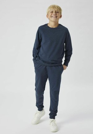 Sweat-shirt bleu marine et joggers assortis en tissu doux. L'ensemble comporte un col ras du cou et des poignets côtelés, associé à des baskets blanches.
