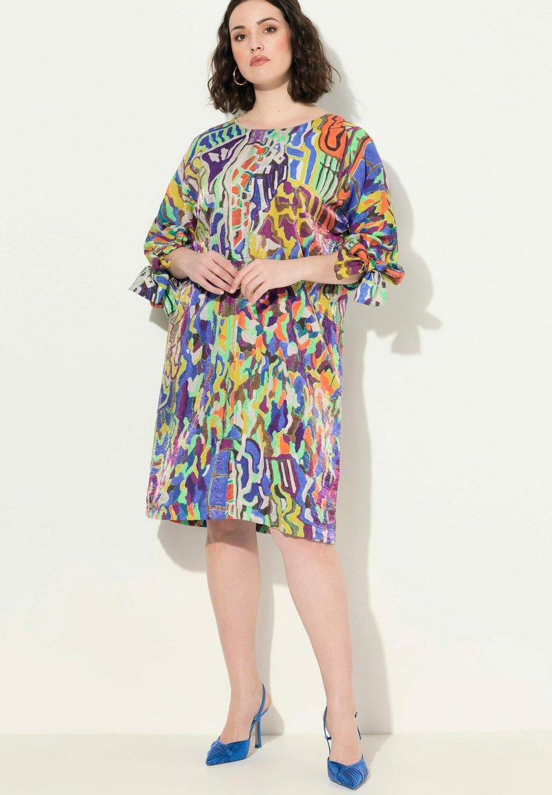 Värikäs kuvioitu mekko, jossa on löysä malli, pyöreä pääntie ja röyhelöhihoja. Yhdistetty sinisiin korkokenkiin.