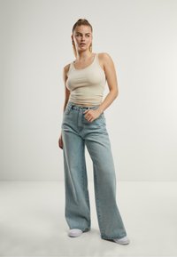 Un top cu bretele ajustat, de culoare bej deschis, asociat cu blugi largi din denim albastru deschis și adidași albi. Design simplu, cu detalii minime.