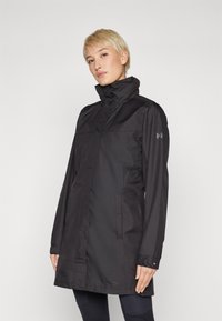 Black waterproof jacket with a high collar and long sleeves. Features a minimalist design, front pockets, and subtle branding on the sleeve.
