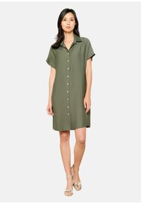 Oliwkowa sukienka koszulowa z krótkim rękawem, z kołnierzykiem, z przodu na guziki, o luźnym kroju, wykonana z lekkiej, teksturowanej tkaniny.