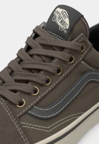 Brown canvas sneaker with gray accents, metal eyelets, flat laces, and stitched detailing. Logo patch on tongue features brand name.