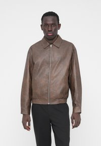 Veste en simili cuir marron avec fermeture éclair, col pointe et ourlet élastiqué. Comprend des poches latérales et des manches longues.