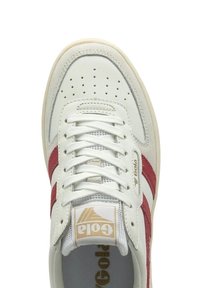 Sneaker in pelle bianca con strisce in suede rosso, punta perforata e linguetta in rete. Presenta lacci piatti e un'etichetta con il logo sulla linguetta.