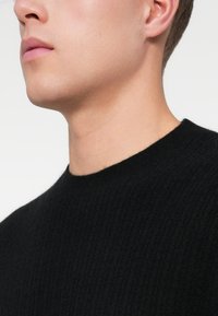Suéter de punto acanalado negro con cuello redondo, que presenta una textura suave y una transición sin costuras del cuello al cuerpo.
