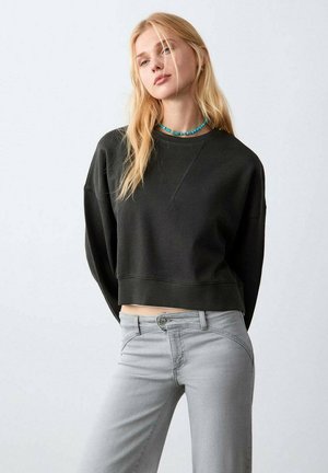 Sweat-shirt noir court avec un col rond et des épaules tombantes, associé à un jean slim gris clair avec des détails de couture subtils.