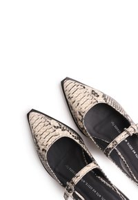 Ballerines à bout pointu avec motif peau de serpent noir et blanc et fines brides à la cheville sur fond blanc.