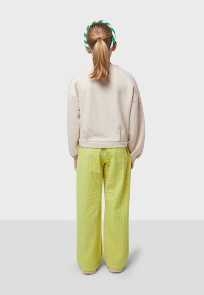 Light pink oversized sweatshirt with a ribbed hem, paired with textured bright yellow checkered pants. Hair is tied back with a green headband.