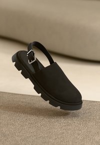 Czarne zamszowe sandały na obcasie z grubą, teksturowaną podeszwą i srebrnym zapięciem. Elegancki design w minimalistycznym stylu, uniesiony nad teksturowaną powierzchnią.