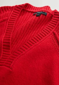 Red knit sweater with a V-neckline and ribbed detailing. Features a textured fabric and a tag labeled "NEXT" at the back.