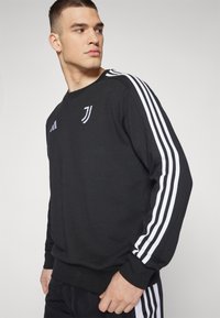 Sort sweatshirts lavet af blødt stof med hvide striber på ærmerne og et lille logo på brystet. Ribbet manchetter og kant.