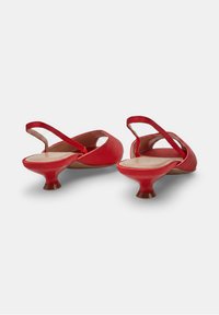 Zapatos rojos de tacón kitten con tira trasera, punta fina y tacones bajos curvos, mostrados desde atrás sobre un fondo blanco.