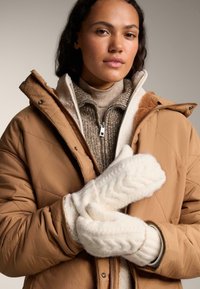 Bežani prešani kaput s smešnim krznom u smešnoj boji, preko rebrastog smešnog džempera smešne boje. Bele teksturirane pletene rukavice s uzorkom kablovske pletenice.