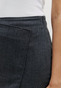 Donkergrijze rok van textuurstof met een zijzak. Heeft een strak ontwerp en een discrete ritssluiting langs de taille.