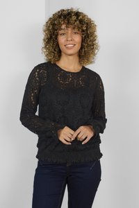 Schwarzes Spitzenoberteil mit langen Ärmeln, das ein gemustertes Design, einen runden Ausschnitt und einen elastischen Saum aufweist. Kombiniert mit dunklen Jeans.