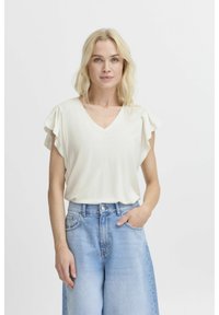 Cream-colored V-neck top with soft ruffled sleeves. The fabric appears smooth, paired with light blue high-waisted jeans featuring pockets.