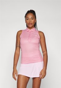Ružový polo top bez rukávov s červeným geometrickým vzorom. Má golier a priliehavý strih. Skombinovaný s skladanou ružovou sukňou.
