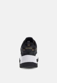 Zwart sneaker met gestructureerde bovenkant en gouden "GUESS" logo, witte tussenzool en patroonaccenten. Heeft een gevoerde schacht en dikke zool.