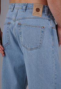 Hellblaue Denim-Jeans mit lockerer Passform, ausgestattet mit einem markierten Lederetikett, Kupferrenndel-Akzenten und Gesäßtaschen mit sanften Nähten.