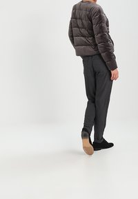 Veste matelassée grise à texture matelassée, associée à un pantalon gris foncé avec des bandes latérales. Chaussures noires complètent la tenue.