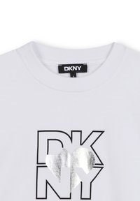 Biała bawełniana koszulka z czarnym napisem "DKNY" i metalicznym srebrnym akcentem w kształcie serca. Okrągły dekolt i krótkie rękawy.