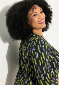 Svart topp med ett livligt grön- och blått abstrakt mönster. Långa ärmar, rund halsringning, tillverkad i ett mjukt tyg med en lätt struktur.