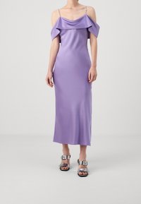 Kobieta w lawendowej, satynowej sukience midi bez ramiączek, z cienkimi paskami i srebrnych sandałach na obcasie z odkrytymi palcami z klamrami.