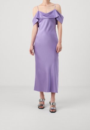 Kobieta w lawendowej, satynowej sukience midi bez ramiączek, z cienkimi paskami i srebrnych sandałach na obcasie z odkrytymi palcami z klamrami.