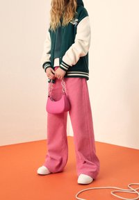 Pantalones anchos de pana rosa, chaqueta varsity verde y crema con puños a rayas, y un pequeño bolso rosa con asa de cadena. Zapatillas blancas.