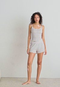 Ensemble de pyjama léger et à motifs composé d'un débardeur blanc à petits pois et d'un short assorti, tous deux avec une coupe décontractée et une texture douce.